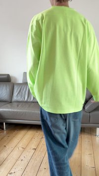 Neon green mesh long-sleeve top with a loose fit and round neckline, paired with blue denim jeans, seen from the back.