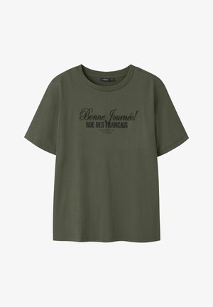 Olive rohelise puuvillane T-särk ümarate kaelaaukudega. Sobilin must printitud tekst: "Bonne Journée! RUE DES FRANÇAIS" ja asutamise üksikasjad.