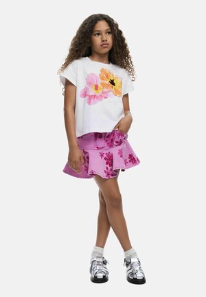 Tricou alb cu mâneci scurte și imprimeu floral, asortat cu o fustă evazată din denim roz cu model floral și sandale argintii.