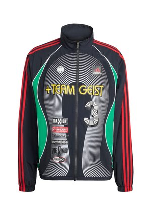 Jūras spēku vējjaka ar sarkaniem svītrām, melniem un zaļiem akcentiem, apaļu baltu rakstu un tekstu "TEAM GEIST". Izceļas ar augstu apkakli un rāvējslēdzēju priekšpusē.