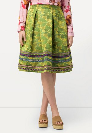 Una gonna verde con motivi a foglie, design plissettato e una banda decorativa colorata all'orlo. Abbinata a sandali con zeppa color sabbia.