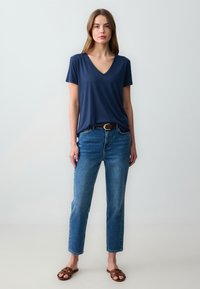 Granatowa koszulka z dekoltem w serek, zestawiona z wysokim stanem niebieskimi dżinsami i brązowymi sandałami. Koszulka ma krótkie rękawy, a spodnie mają prostą nogawkę.