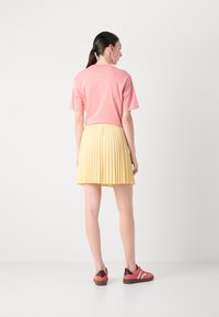 T-shirt rosa a maniche corte, gonna gialla plissettata, sneakers rosa e marroni. Design semplice, tessuto leggero, pieghe visibili sulla gonna.