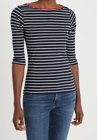 Navy striped long-sleeve top with white horizontal stripes and a red neckline. The fabric appears soft and fitted, paired with blue jeans.