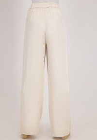Wijde broek van een zachte beige stof, met een elastische tailleband en een gladde textuur. Het ontwerp benadrukt een losse pasvorm en een vloeiende silhouet.
