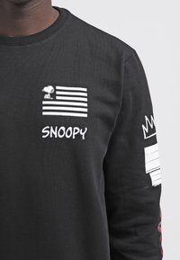 Felpa nera con Snoopy ricamato e strisce orizzontali. Include la parola "SNOOPY" e accenti grafici sulle maniche.
