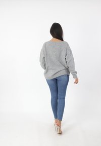 Maglione grigio oversize con orlo a coste, scollatura leggermente off-shoulder, abbinato a jeans blu aderenti e sandali con tacco trasparente.