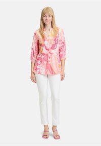 Chemisier léger à motif en rose, orange et blanc, avec un col à boutons et des manches trois-quarts, associé à un pantalon blanc et des sandales roses.