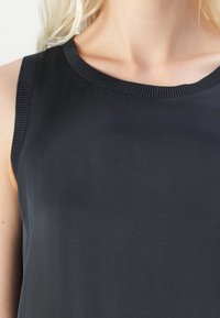 Top fără mâneci de culoare bleumarin, cu un guler rotund și margine ribbată, având o textură netedă și moale. Potrivit pentru purtarea zi de zi.