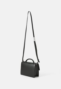 Sac à bandoulière en cuir noir de forme rectangulaire, avec une poignée supérieure et une sangle ajustable. Texture lisse et design minimaliste.
