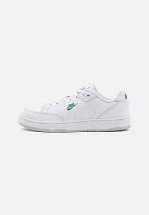 Sapatilhas brancas de pele com uma textura suave, apresentando um logo Nike verde, sola cinza e elementos de design minimalistas.