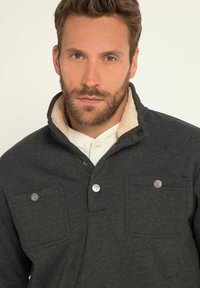 Pullover grigio scuro con un morbido colletto color avorio, due tasche frontali e dettagli con bottoni. Realizzato in tessuto testurizzato con una vestibilità comoda.