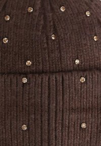 Beanie lavorato a maglia marrone con texture a coste, caratterizzato da abbellimenti riflettenti leggeri distribuiti per un tocco di dettaglio in più. Materiale caldo e morbido.