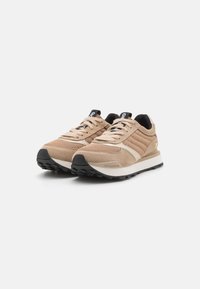 Beige treningsko med en teksturert semsket skinn og mesh overdel, gummisåle, svarte lisser og minimal merking på sidene og tungen.