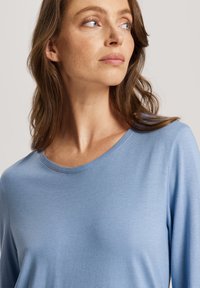 Blusa de manga larga azul claro con escote redondo, textura suave y un corte casual, adecuada para diversas ocasiones.