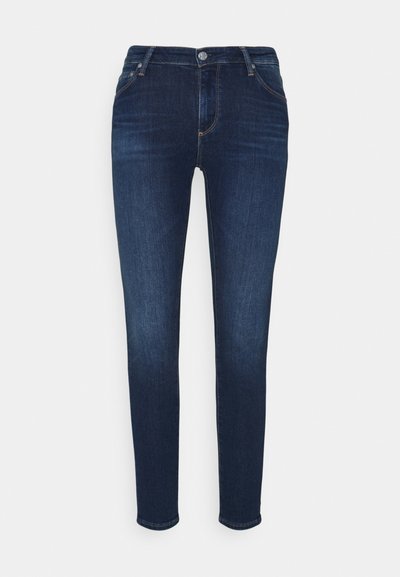 Calças de ganga azul-escuro com um corte slim, design de cinco bolsos, desgaste subtil e fecho de botão metálico na cintura.