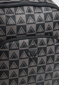 Zaino nero e grigio con motivo geometrico a triangoli, realizzato in materiale sintetico liscio e dotato di chiusura superiore con cerniera.