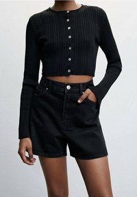 Černý žebrovaný pletený zkrácený cardigan s knoflíkovým zavíráním, ve spojení s černými džínovými kraťasy vysokého pasu s předními kapsami a zipem.