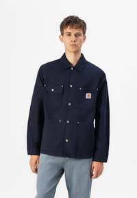 Chaqueta azul marino con cuello tipo solapa, dos bolsillos en el pecho y botones de presión. Fabricada con un tejido duradero y de textura suave.