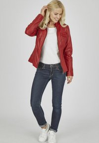 Rote Lederjacke mit hohem Kragen und Reißverschluss, kombiniert mit dunkelblauen Jeans und weißen Sneakers. Glatte Textur, taillierte Passform.