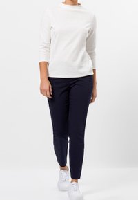 Top bianco a maniche lunghe con texture, abbinato a pantaloni aderenti blu navy e sneakers bianche. Il design presenta un collo alto e una silhouette slim fit.