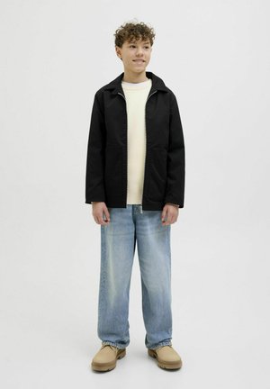 Veste légère noire avec col, pull clair en dessous, jeans oversized bleus et chaussures beiges. Design simple et coupe décontractée.