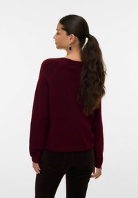 Maglione bordeaux in morbido tessuto a maglia con spalle cadenti; polsini e orlo a costine; abbinato a pantaloni in velluto a coste scuri.