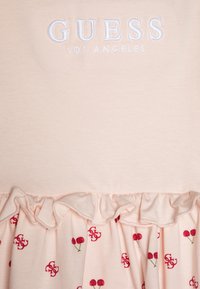 Różowa bawełniana sukienka z haftowanym napisem "GUESS LOS ANGELES", falbanami u dołu oraz wzorem czerwonych wiśni z zielonymi łodygami.