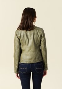 Giacca in pelle verde oliva con finitura texturizzata, design aderente e dettagli cuciti. Abbinata a jeans in denim blu scuro.