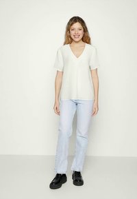 Top branco em tecido leve com decote em V e mangas curtas, combinado com jeans de perna reta azul claro e sapatos de plataforma pretos.