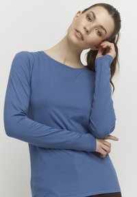 Langärmliges, eng anliegendes Oberteil in gedämpftem Blau, aus weichem Material. Verfügt über einen runden Ausschnitt und eine glatte Textur, ideal zum Kombinieren.