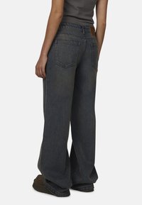 Des jeans en denim foncé à jambes larges présentent une taille haute, une ceinture élastique et des poches arrière. Le tissu a une finition légèrement texturée.