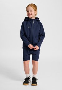 Mörkblå huva med dragkedja framtill, korta mörkblå shorts och svarta skor med gummisula. Jackan har en logotyp.