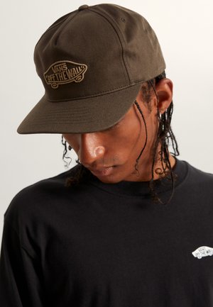 Gorra de color marrón oscuro hecha de tela, con un logo "Off the Wall" de color marrón claro bordado. Visera curvada, diseño de seis paneles y ojales transpirables.