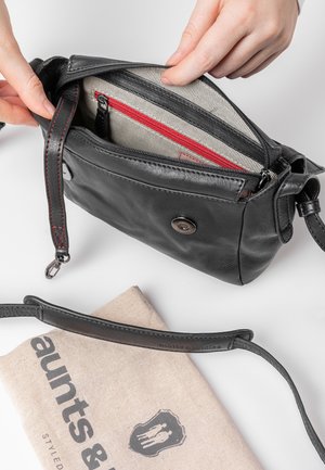 Black leather crossbody bag with a zippered closure, striped lining, red accents, and exterior snap button. Includes a fabric dust bag.