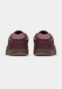 Ζευγάρι μπορντό σουέτ αθλητικά παπούτσια με ροζ ταμπελάκια στη φτέρνα που δείχνουν "1973" και καφέ σόλες με ανάγλυφο το όνομα "Pepe Jeans", εικόνα από πίσω.