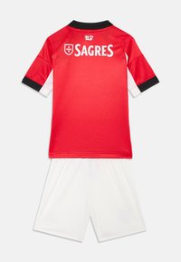 Raudona futbolo marškiniai su juodais ir baltais akcentais, kuriuose ant nugaros yra užrašas "SAGRES"; derinami su baltais šortais, pagamintais iš lengvos medžiagos.