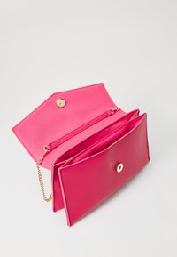Jasně růžová kabelka s klopou a zlatým řetízkem, magnetickým uzávěrem a vnitřními přihrádkami na bílém pozadí.