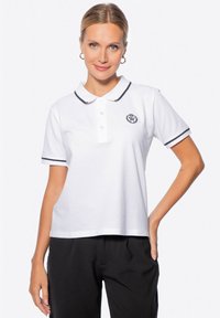 Camisa polo blanca con ribete negro en el cuello y las mangas, con una tapeta de tres botones y un logotipo circular en el lado izquierdo del pecho.