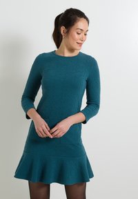 Vestido verde azulado hecho de tela texturizada, con un escote redondo, mangas de tres cuartos, dobladillo acampanado y dos bolsillos al frente.