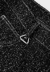 Zwarte gestructureerde stof met witte spikkels; beschikt over een metalen haak die aan de tailleband is bevestigd, met zichtbare stiksels.