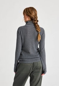 Pulover gri cu guler rulat, cu textură cu nervuri, mâneci lungi, design ajustat, asortat cu pantaloni lejeri de culoare verde măsliniu.