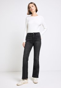 Jeans neri a campana con vita alta e tasche frontali, abbinati a una maglietta aderente a maniche lunghe bianca e sneakers color crema. Tessuto dalla texture liscia.
