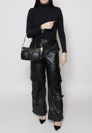Woman wearing black turtleneck and black leather cargo pants, holding black leather handbag with front pockets, and wearing black pointed heels.