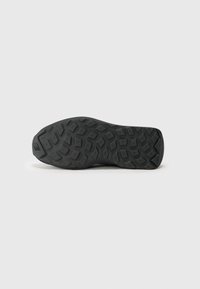 Semelle de chaussure en caoutchouc noir avec un motif de semelle multi-directionnel et une surface texturée pour une meilleure adhérence, comportant un logo sur la zone du talon.