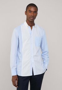 Camicia a righe azzurro chiaro con inserto bianco, colletto e taschino sul petto. Presenta righe sottili e larghe in contrasto.
