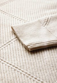 Beige gebreide stof met een ribbelstructuur en diagonale lijnen, voorzien van een omgeslagen manchetdetail, dat zacht en comfortabel materiaal toont.