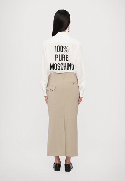 Hvid skjorte med sort tekst "100% PURE MOSCHINO" på ryggen, parret med en beige højtalje nederdel og sorte flade sko.