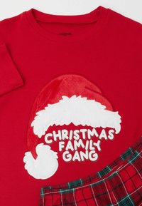 Czerwona bawełniana koszulka z nadrukiem białej, puszystej czapki Mikołaja i napisem "CHRISTMAS FAMILY GANG" w grubych literach. Zawiera akcenty w kratę.