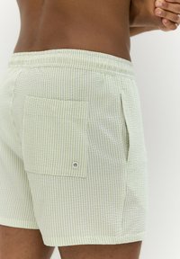 Világoszöld, kis kockás mintájú rövidnadrág. Rugalmas derékpánt hátul egy gombos zsebbel. Pamut anyag, laza szabású.